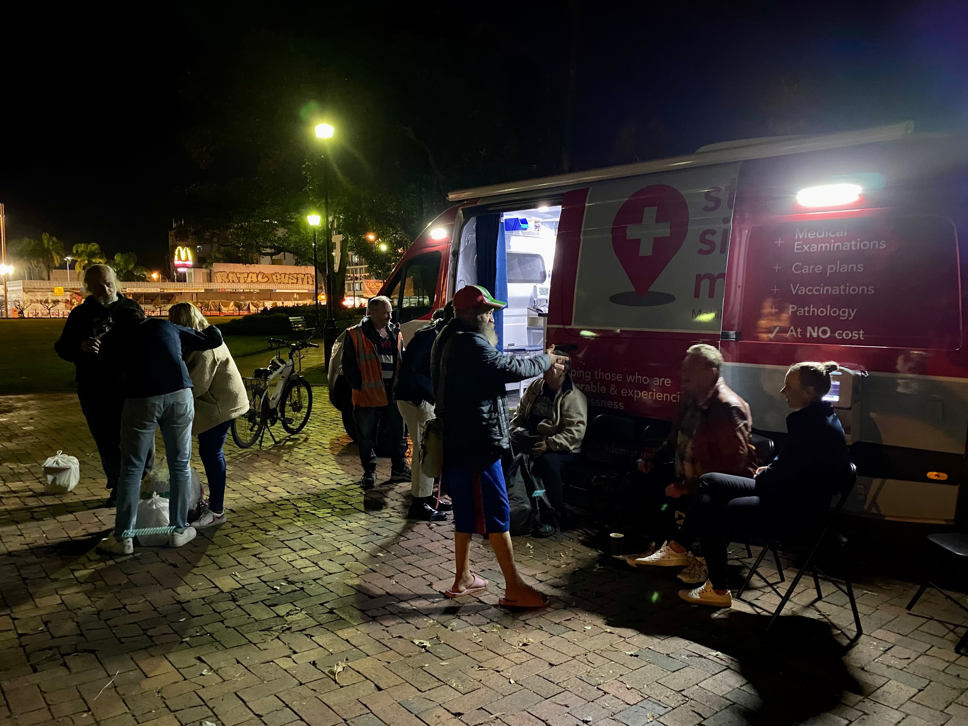 A group of people sit and stand outside a van at night.