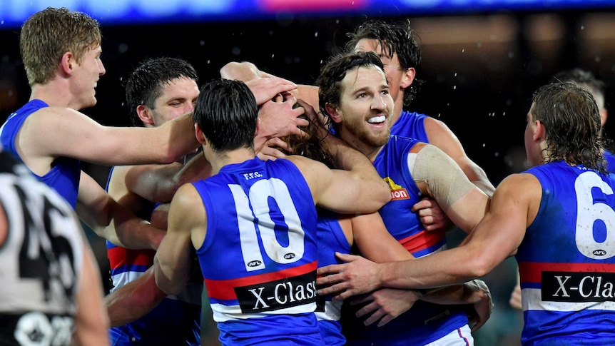 A group of AFL players tousle the hair of a goalscorer as the rain falls at Adelaide Oval.