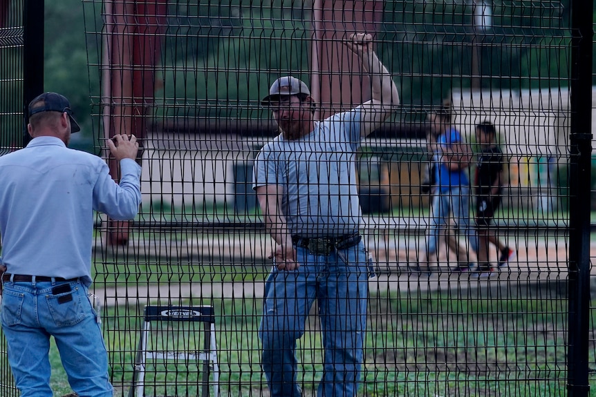 Two men carry a large piece of metal fence. 