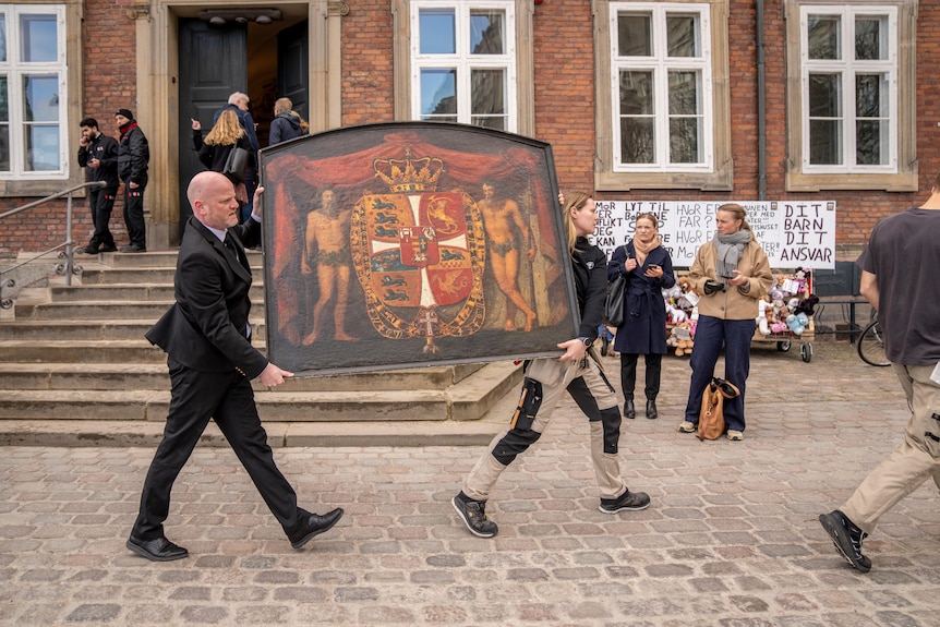 A man and a woman carry a historical painting down the street.