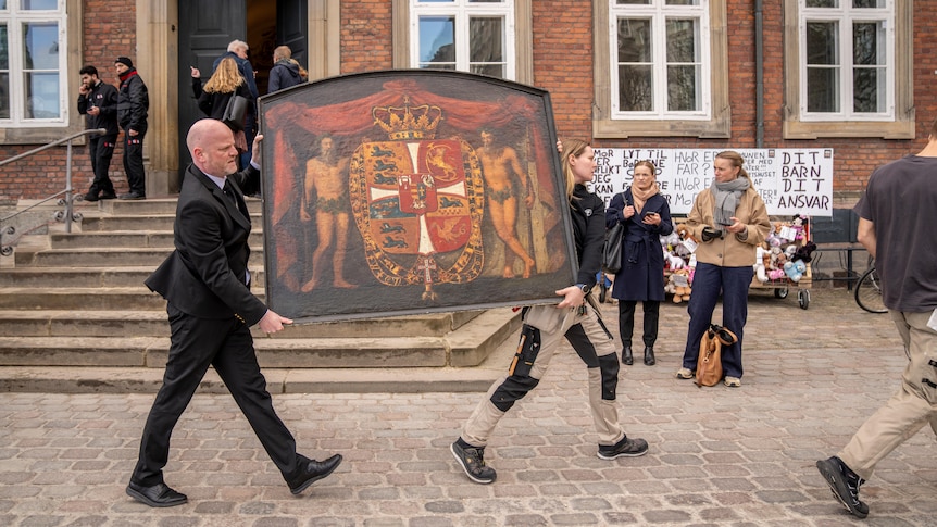 A man and a woman carry a historical painting down the street.