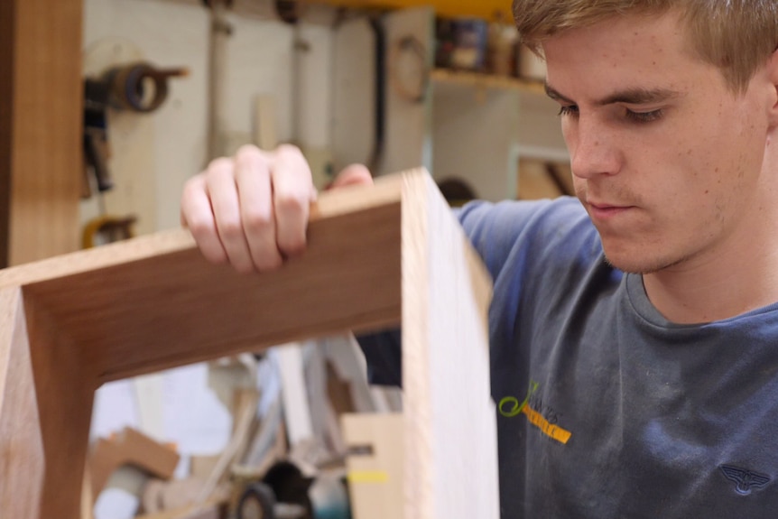 A young man holds a piece of timber.