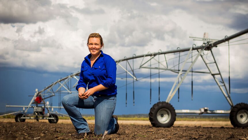 A woman kneeling down on soil in front of a large irrigator.