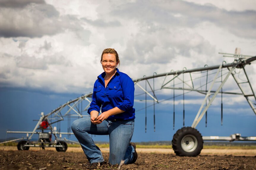 A woman kneeling down on soil in front of a large irrigator.
