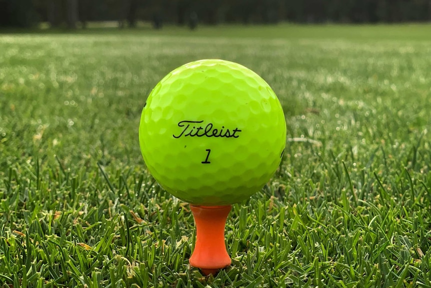 A fluro yellow golf ball sitting on a yellow tea on a lush green golf course.
