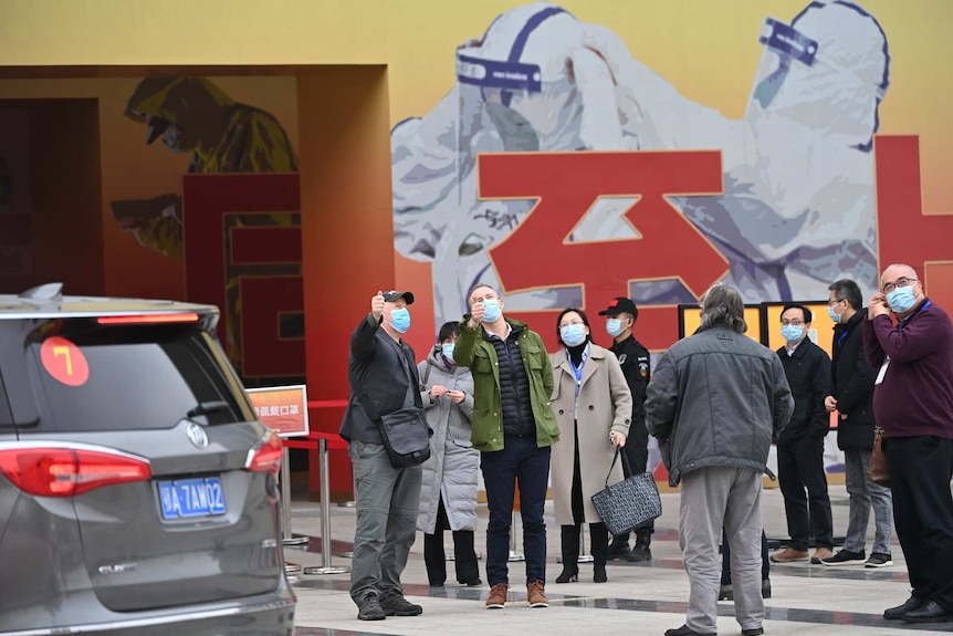 Adults wearing masks standing in front of a mural of people wearing personal protective equipment