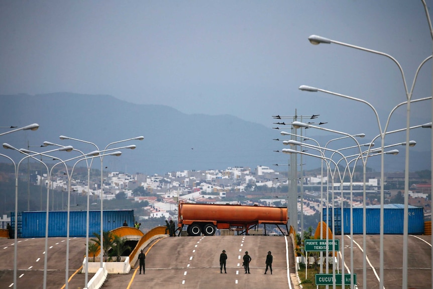 Truck containers are spread across a highway as soldiers stand guard at the Venezuelan border.