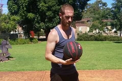 Jason Colton, a man wearing a singlet and shorts, holds a black basketball in one hand.