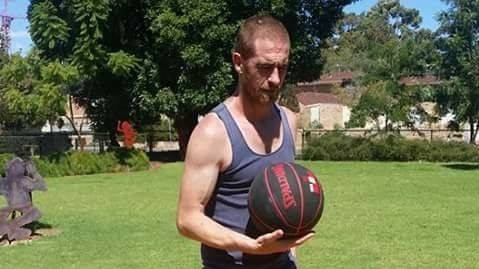 Jason Colton, a man wearing a singlet and shorts, holds a black basketball in one hand.