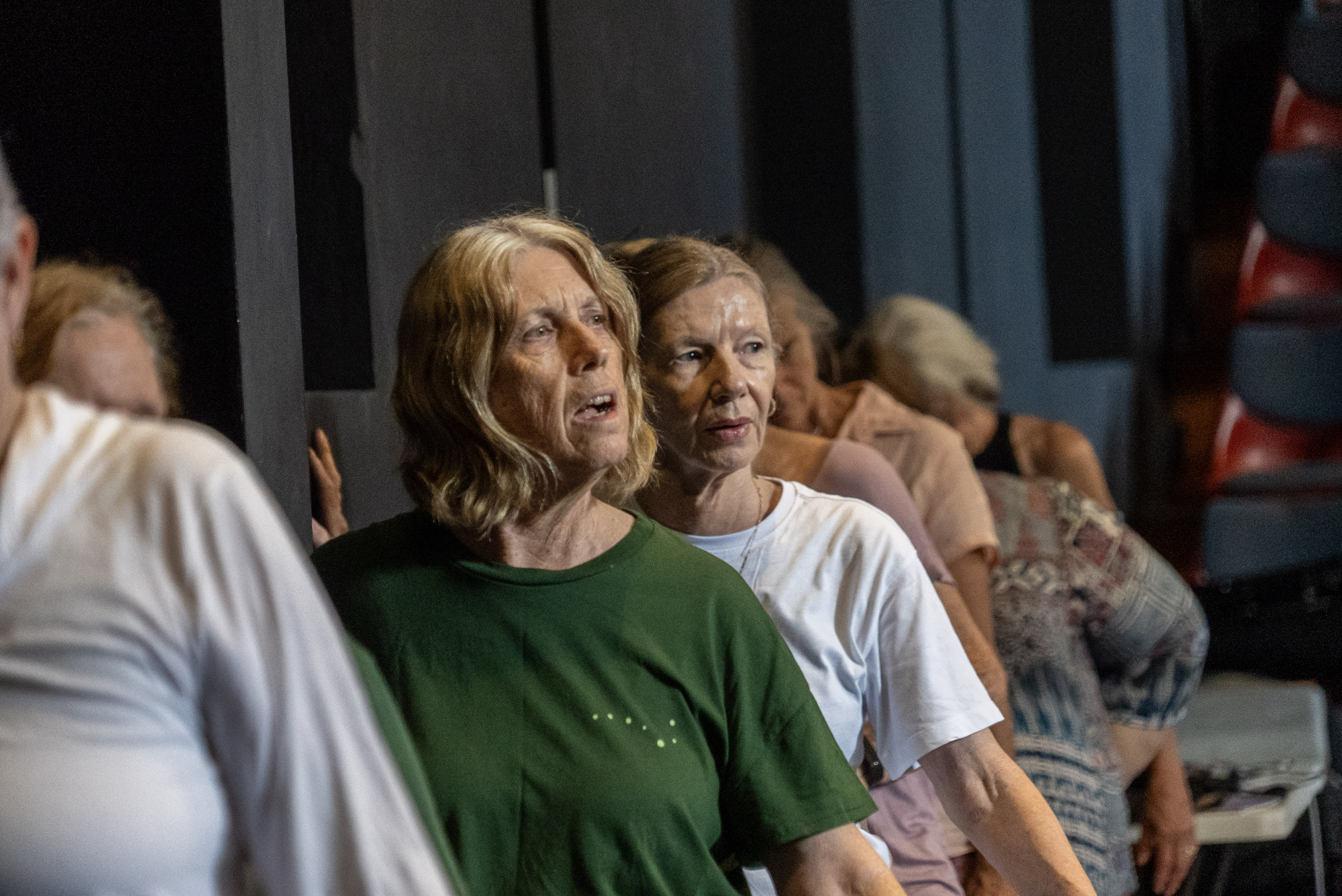 A line of six women lean with one hand up against a wall practicing a dance. 