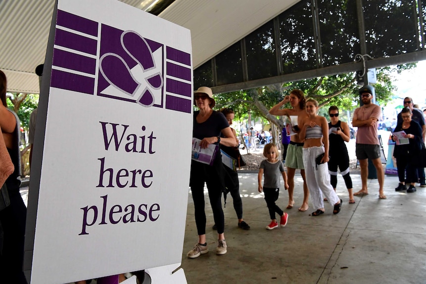 People queue to cast their vote in front of a 'Please wait here' sign