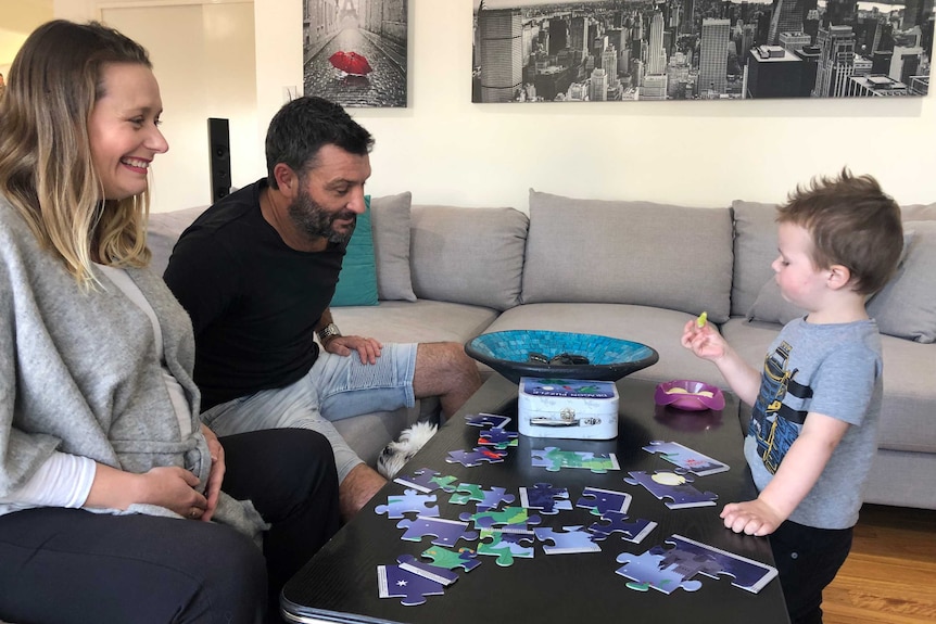 A mother and father sit on a lounge putting together a jigsaw puzzle with their young son.
