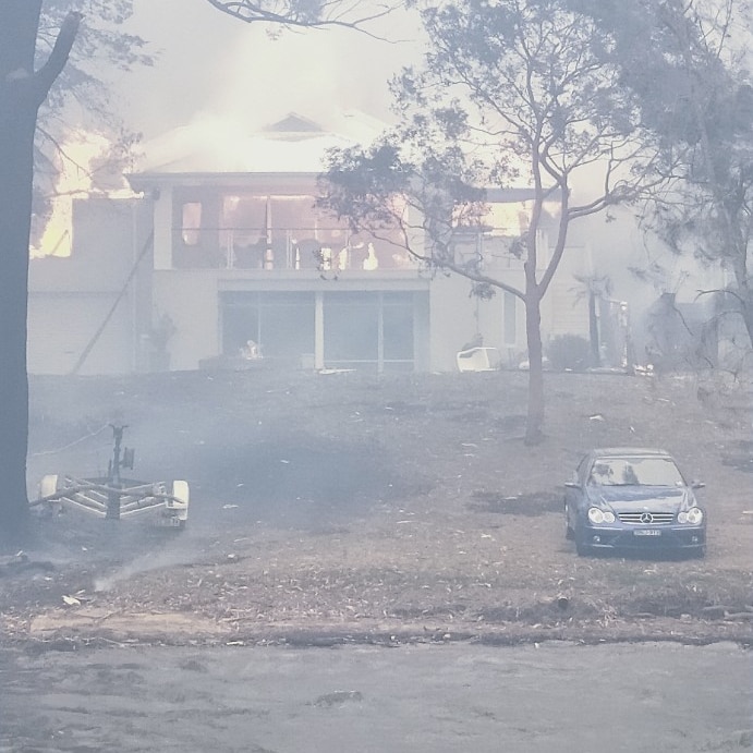 A two-storey house is engulfed by flames with water in the foreground, indicating the photographer was on the water.