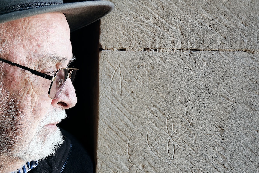 Man examines hexafoil markings on a wall in Tasmania.