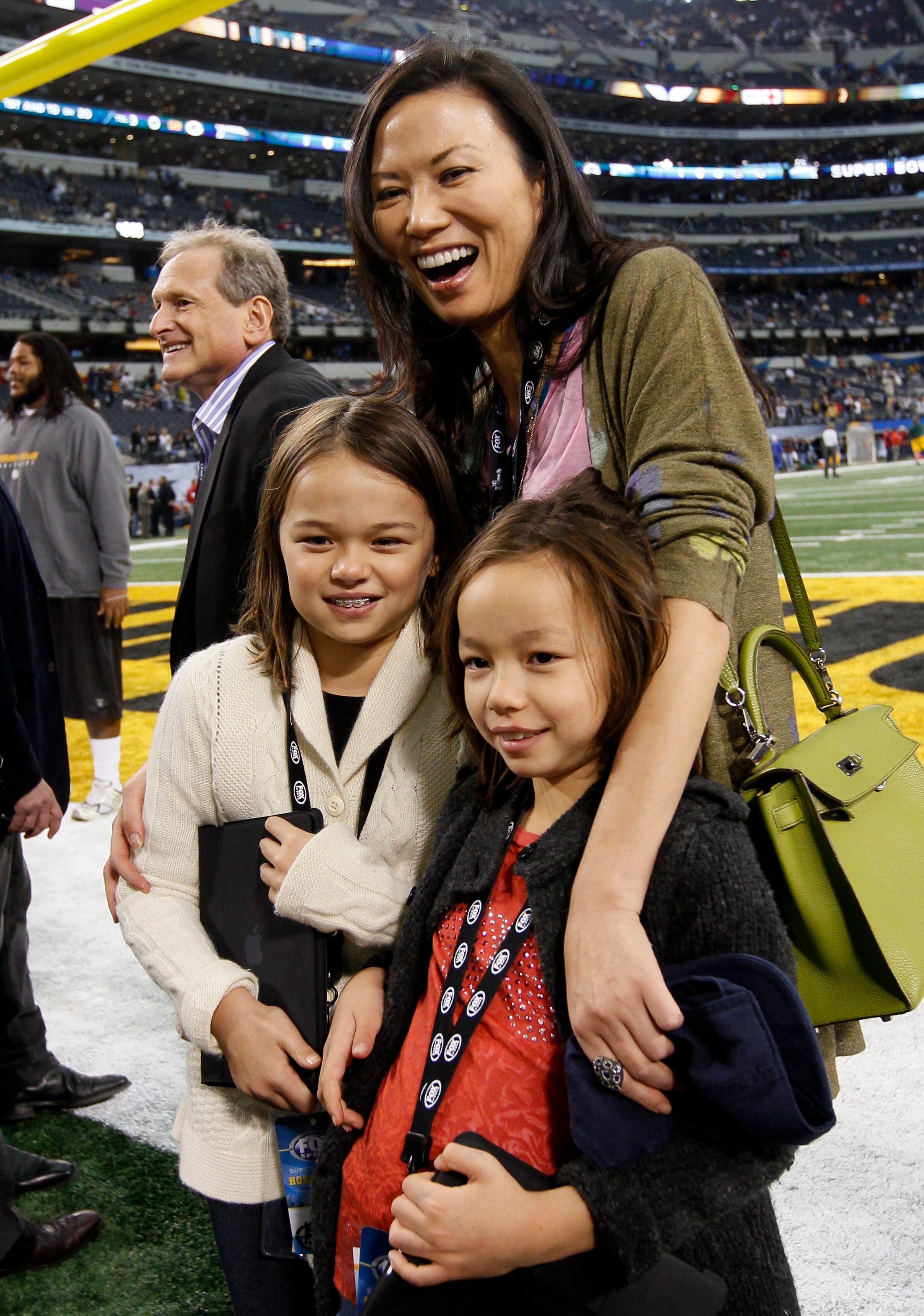 Wendi Deng laughing on a football field with her arm around two little girls 