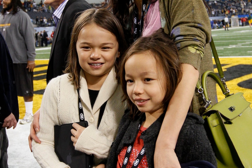 Wendi Deng laughing on a football field with her arm around two little girls 