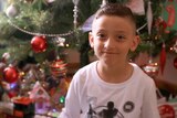 A young boy smiles in front of a Christmas tree.