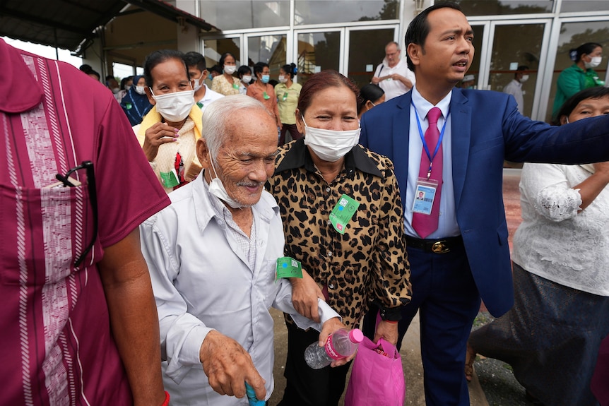 An elderly man standing with support outside a court