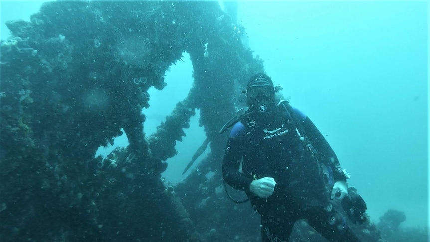 A diver underwater with the wreck of a ship.
