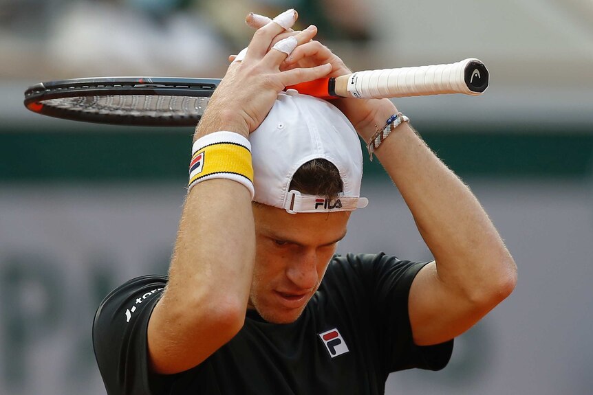 Diego Schwartzman looks down and places his racket and hands on his head.