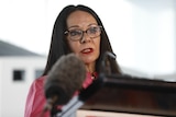 Linda Burney at a lectern with a large microphone in front of her. 