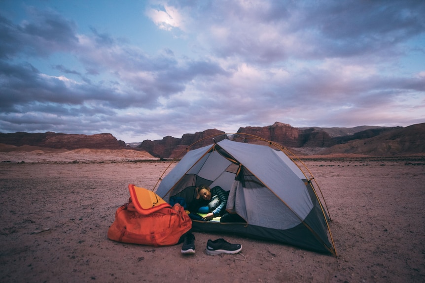 Mina Guli lies in tent in barren landscape with rocky range in background during sunset.