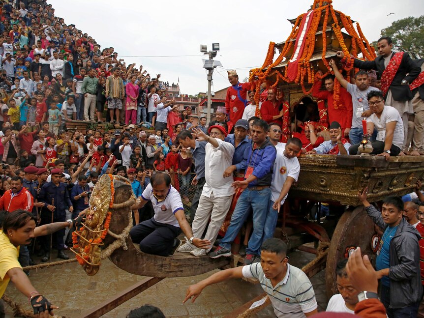 A mass of people watch a colourful chariot being pulled through the street
