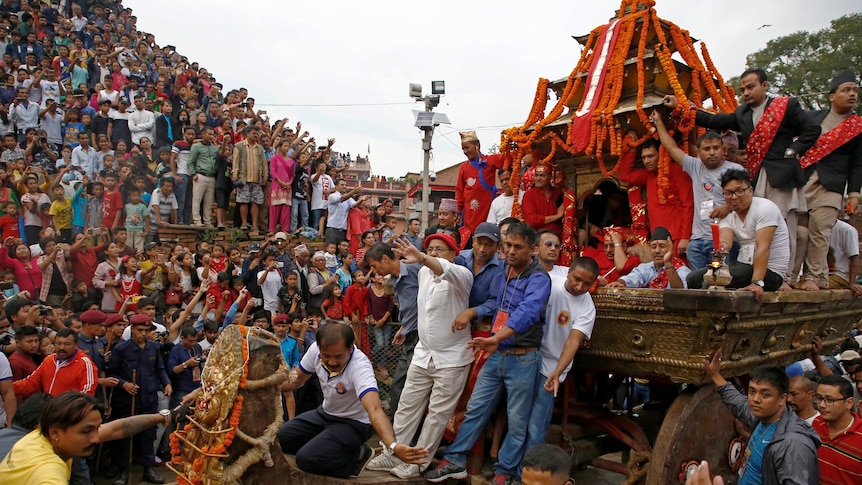 A mass of people watch a colourful chariot being pulled through the street