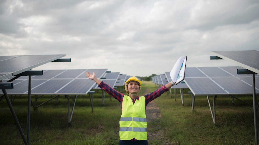 Woman with arms outstretched standing in front of solar panels