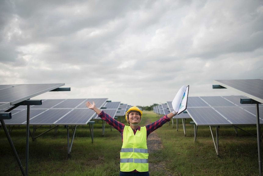Woman with arms outstretched standing in front of solar panels