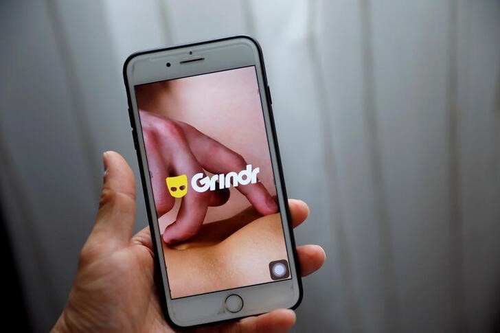 a hand holding a smartphone which has gay dating app Grindr logo showing