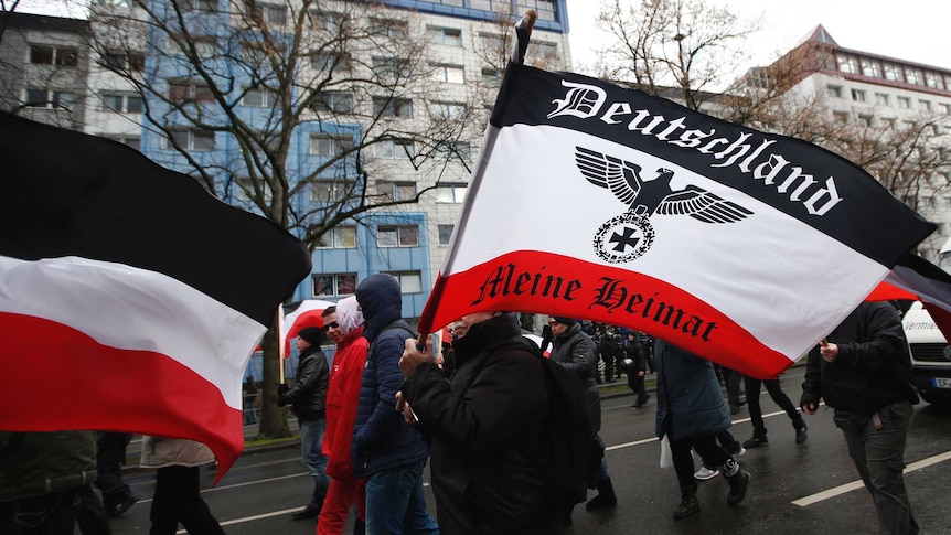 You view a grey street with a crowd of far-right supporters marching through the streets in black and the German Imperial flag.