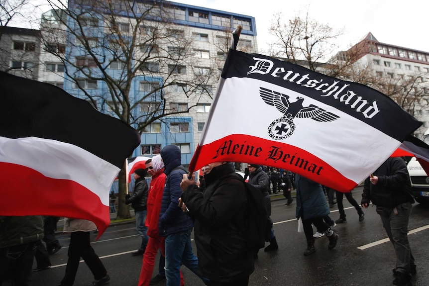 You view a grey street with a crowd of far-right supporters marching through the streets in black and the German Imperial flag.