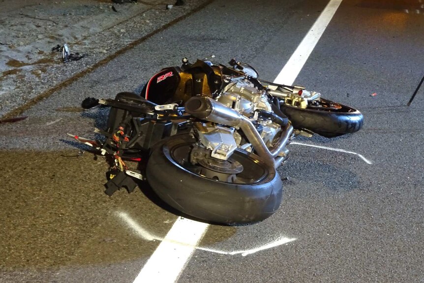 A crashed motorbike lies on the side of the road.