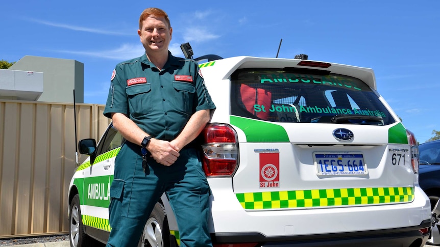 A man in paramedic uniform leaning against an ambulance.