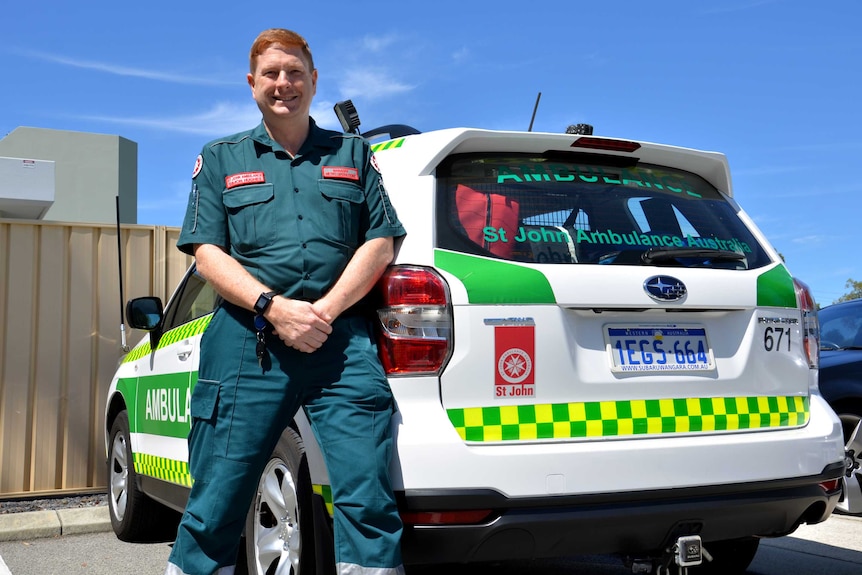 A man in paramedic uniform leaning against an ambulance.