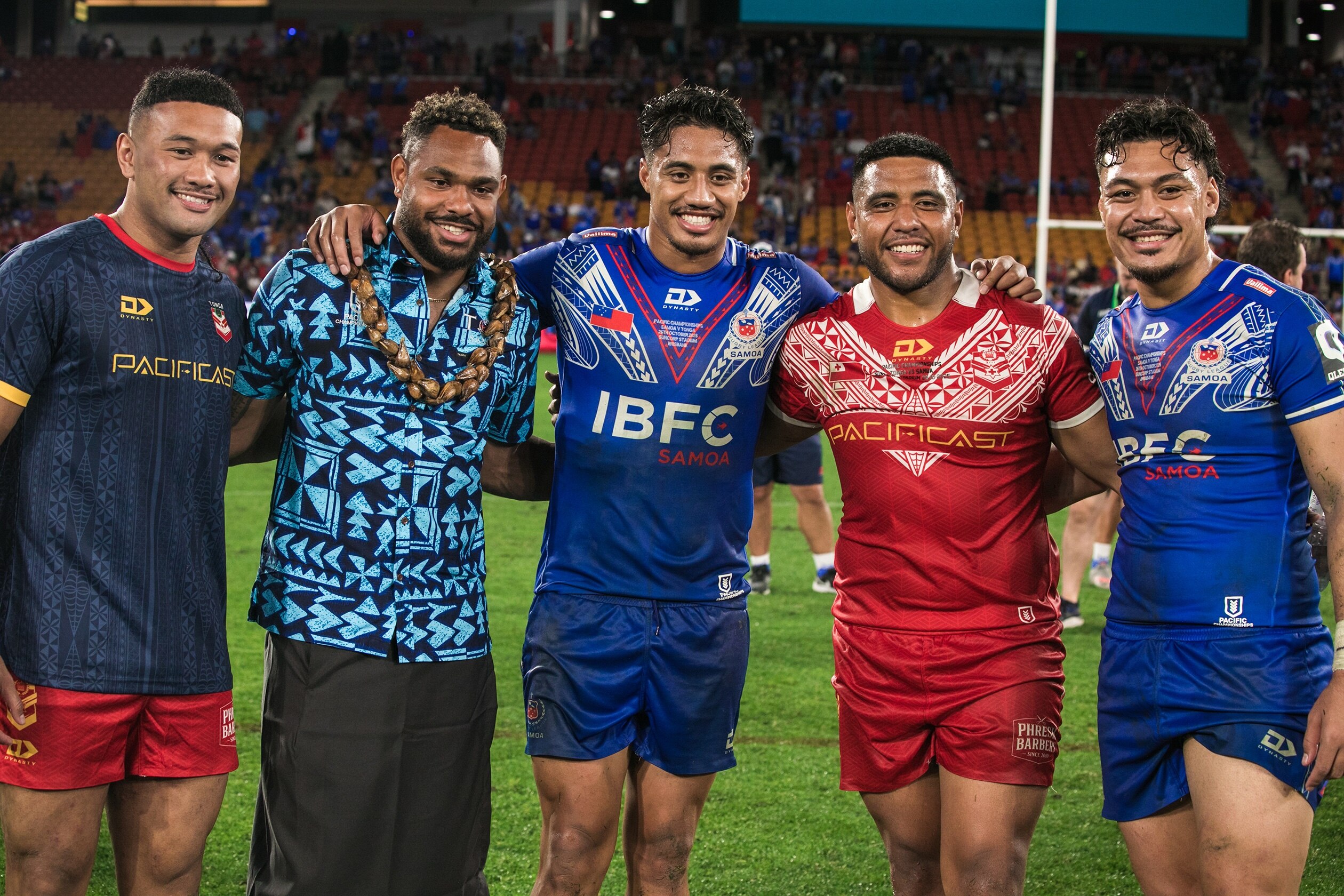 3 men in blue Samoan rugby league uniforms stands with another 2 men wearing red and grey Tongan rugby league uniforms on field