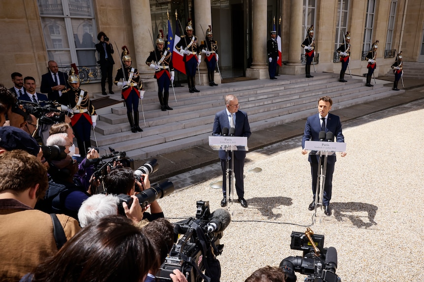 A ceremonial guard and a group of reporters and photographers look on as two men hold a press conference