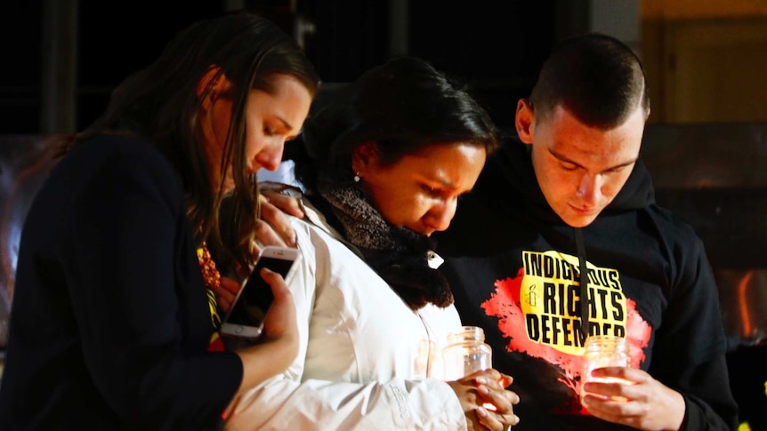 Three people look down at their candles at a protest.