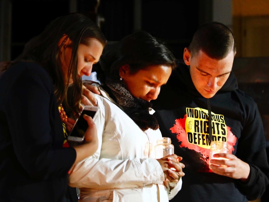 Three people look down at their candles at a protest.