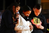 Three people look down at their candles at a protest.