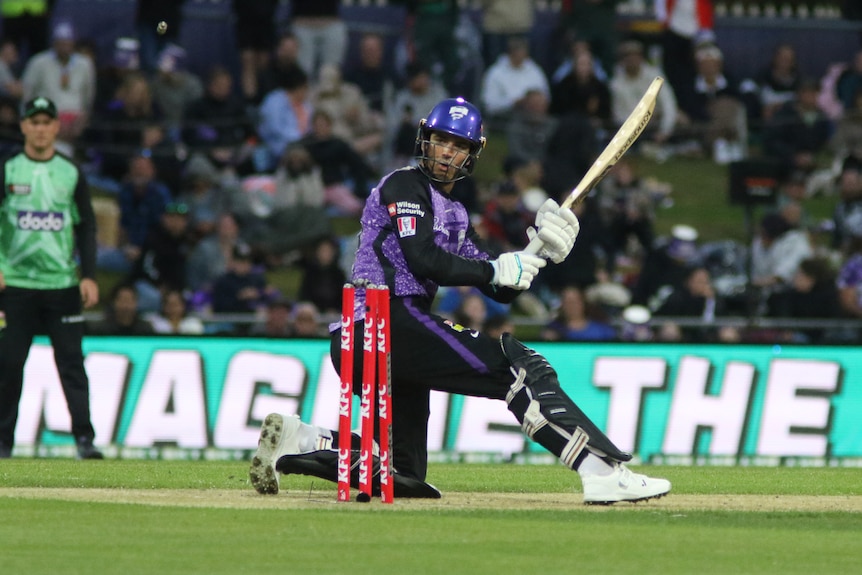 a man in a purple cricket uniform and helmet is swinging a bat mid-game