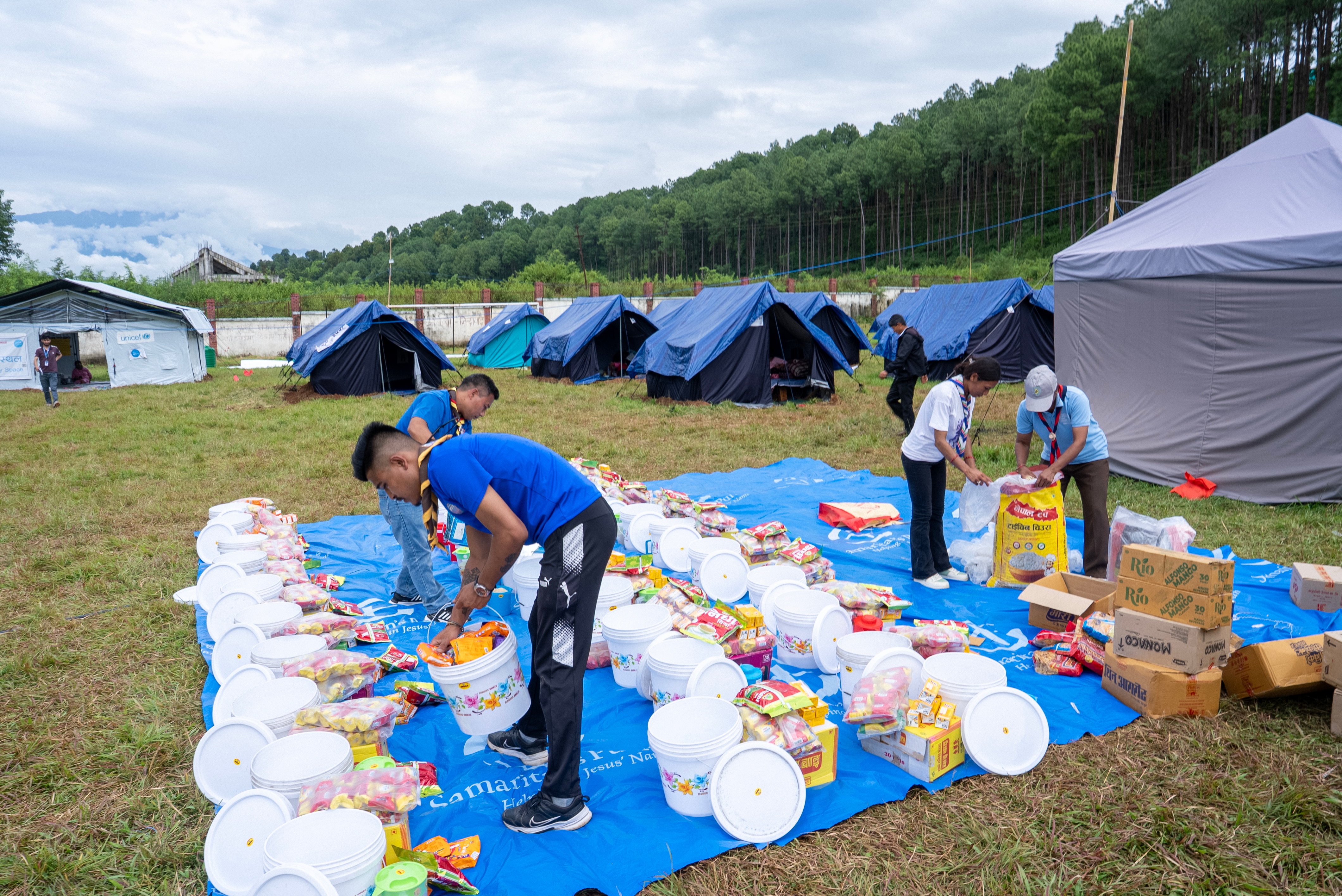 On a large blue tarpaulin, 5 aid workers lay out rows of food and supplies.