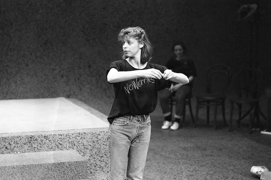 A black and white image of a woman on stage wearing a T-shirt and jeans