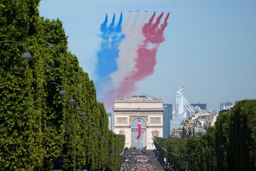Nine jets fly over the Arc de Triomphe, with a trail of blue white and red coming out of the jets. 