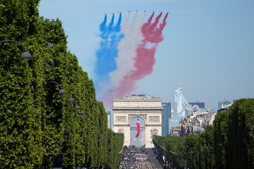 Nine jets fly over the Arc de Triomphe, with a trail of blue white and red coming out of the jets. 