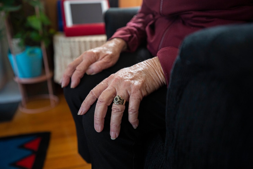 An elderly woman rests her hands on her knees