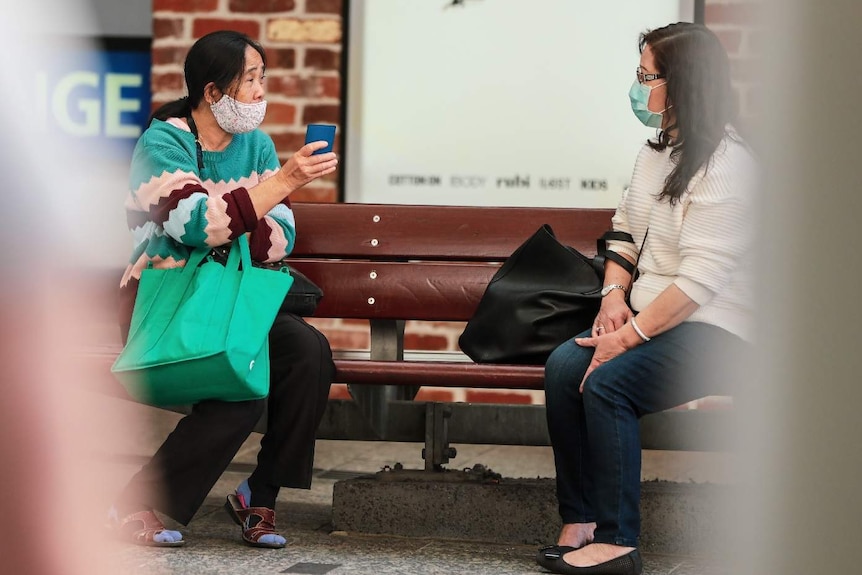 Two women in masks socially distanced on a bench