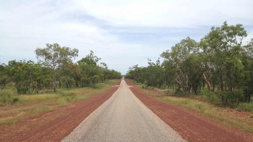 A single lane road flanked by thick scrub in the Northern Territory
