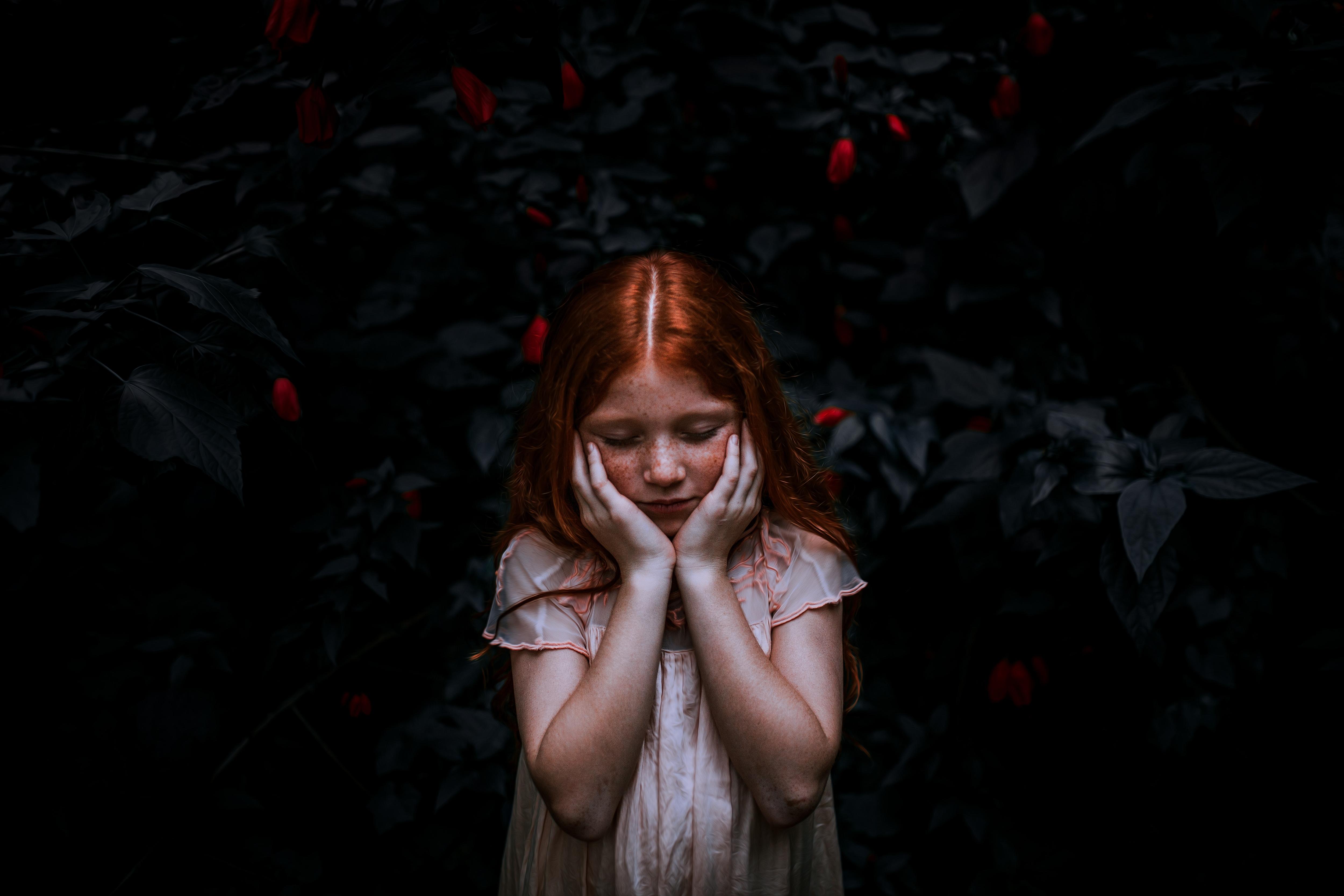 A moody photo of a pale young girl with red hair holding her head in her hands